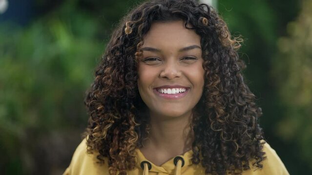 Portrait of a happy black hispanic young woman looking at camera. Young African American latina with curly hair standing outdoors smiling