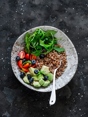 Healthy balanced vegetarian breakfast - buckwheat with avocado, arugula, cherry tomatoes and blueberries on a dark background, top view