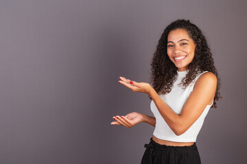 Young Brazilian black woman presenting with her hands to the left, publicity photo.