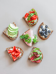 A variety of breakfast, tapas, snack sandwiches - with avocado, cream cheese, ham, berries, salami, cherry tomatoes on a light background