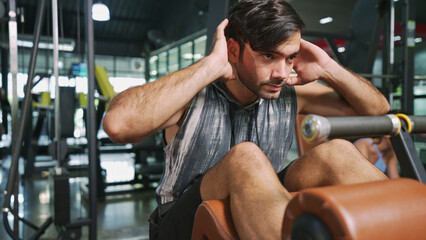 Portrait of Asian male bodybuilder lying down sit-up bench and doing sit-up workout to maintain core muscles. Athlete man concentrate on posture and control abs muscles. Bodybuilding at gym concept