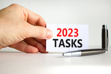 2023 Tasks symbol. White paper with words 2023 Tasks. Businessman hand. Metallic pen. Beautiful white table white background. Business and 2023 tasks concept. Copy space.