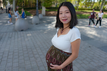 Fototapeta premium young happy and beautiful Asian Chinese woman posing outdoors happy and cheerful pregnant showing her belly proud smiling in pregnancy and maternity concept