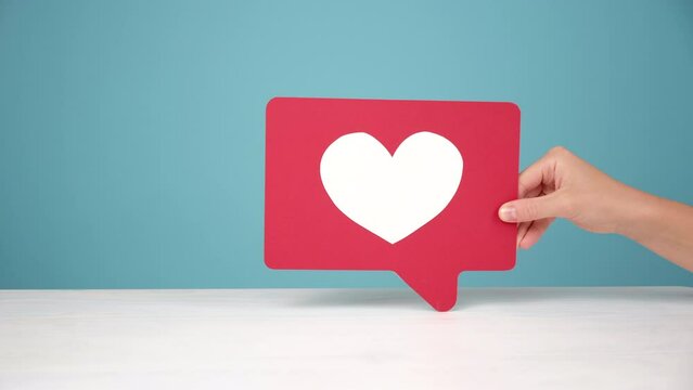 Appreciate content with heart button. Closeup of female hand holding like icon of social media at desk, emoji sign to follow subscribe interesting blog, popular forum, posing on blue background wall