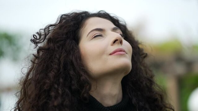 Young woman looking up at sky with HOPE. Contemplative 30s girl standing outdoors raises looks up smiling