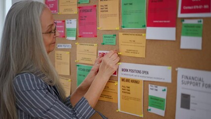 Job center employee pinning job vacancies on employment noticeboard.