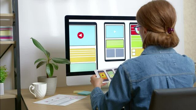 A woman web designer is working on the creation of an application interface for a mobile phone using a computer. User experience