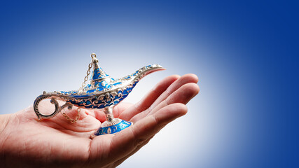 Aladdin's magic lamp in a woman's hand on a pale blue background. Arabian fairy tales, magic. Symbol of good luck, wealth. Advertising, banner, invitation.