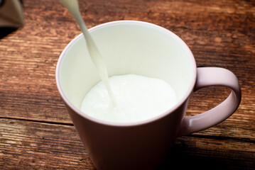 Milk is poured into a cup on a brown wooden background.