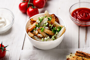 Fried potatoes in a white plate with green onions, ketchup on a white wooden background.