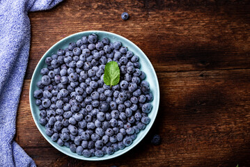 Fresh blueberries berries in a plate on a dark wooden background.