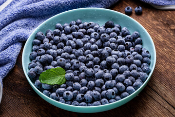Fresh blueberries berries in a plate on a dark wooden background.