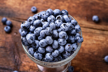 Fresh tasty blueberries in a glass bowl on a dark wooden background.