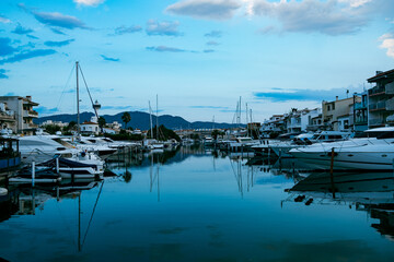 Fototapeta na wymiar Empuriabrava spanish town in view of main water channel with boats at dusk. Landscape of the catalan town in the Costa Brava region known for its canals and marina