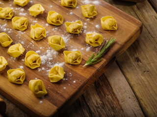 Close-up. Cooking homemade dumplings stuffed with minced meat. Raw homemade dumplings on a wooden cutting board sprinkled with flour and a sprig of rosemary.