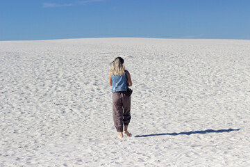 a girl walks alone in the desert along a sand dune, white sand on a sunny day