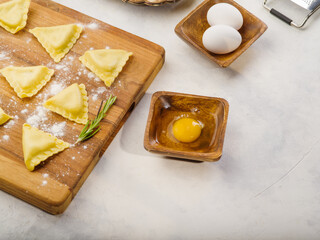 Cooking homemade Italian ravioli on a wooden cutting board on a white background. Raw ravioli, ingredients and kitchen utensils. Healthy lifestyle, delicious organic food.