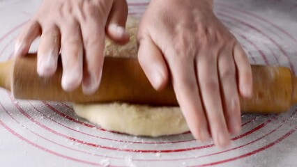 Female hands roll out yeast dough on a silicone mat with a wooden rolling pin. Loose, smooth dough for making bread and bakery products