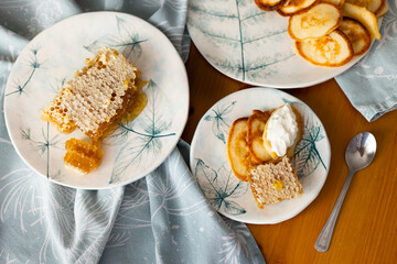 Homemade small pancakes with sour cream and honey in honeycombs on light blue plates