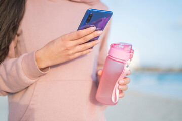 girl holding phone smartphone in hands on the seashore and sport bottle with water