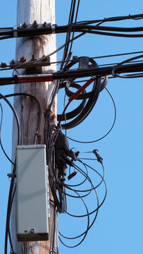 Utility pole with fiber optic cables and junction box, and clear blue sky. 