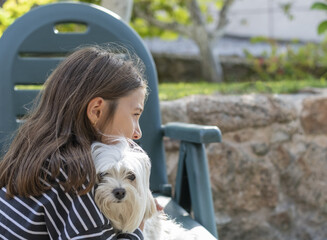 Side view of a girl hugging a Bichon Maltese dog.