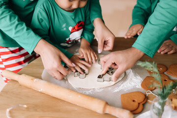 An Asian family with two children in green pajamas cook together festive cookies celebrate the...