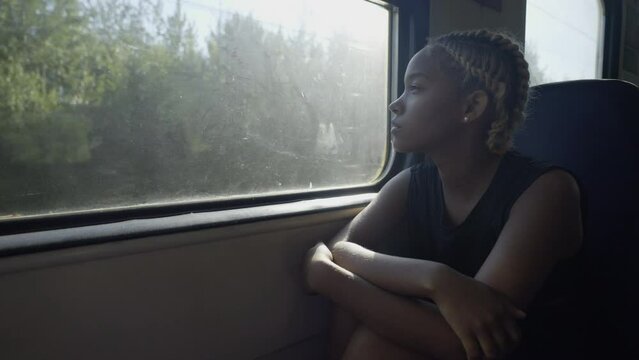 A young woman with blond hair and pigtails sits in an electric train and looks thoughtfully out the window. Slow motion 4k footage