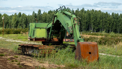 Fototapeta premium green excavator, green grass in the swamp on a very sunny day. Rusty chains and cup