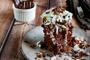 Piece of chocolate american pie with condensed milk icing, medal flakes and grated chocolate on top, brown tones, appetizing sweet dessert