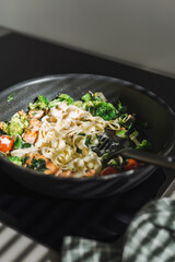 Fettuccine with salmon and vegetables in a creamy sauce in a pan on the stove.