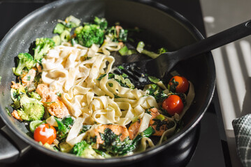 Fettuccine with salmon and vegetables in a creamy sauce in a pan on the stove.