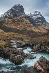 Fototapeta na wymiar Epic landscape image of vibrant River Coe flowing beneath snowcapped mountains in Scottish Highlands