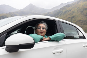 A gray-haired lady in a car in the driver's seat against the backdrop of the Alpine mountains
