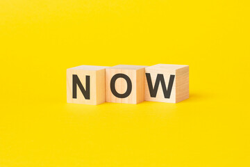wooden blocks with text NOW on yellow background. business concept