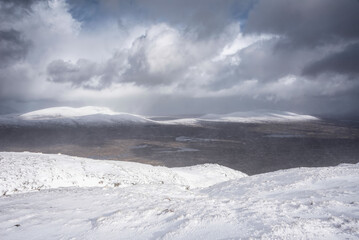 Fototapeta na wymiar Epic Winter landscape image from mountain top in Scottish Highlands down towards Rannoch Moor during snow storm and spindrift off mountain top in high winds