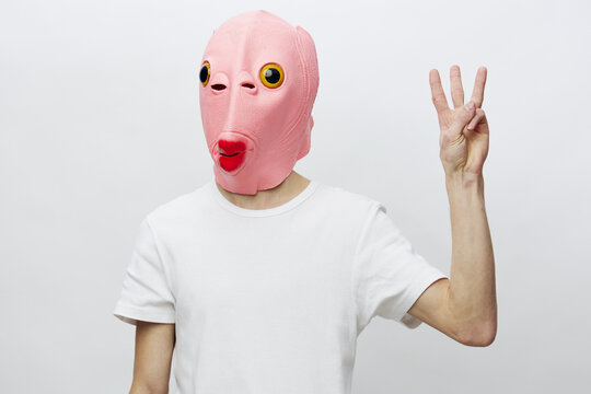 portrait of a man in a pink mask on his face showing numbers with his fingers looking at the camera