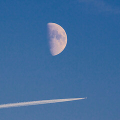 Flight under moon, white plane trail in blue sky