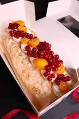 Meringue roll with cream cheese cream in a white box, roll garnished with fresh berries. Fruits decoration, red currant, kumquat, dessert for the gift.