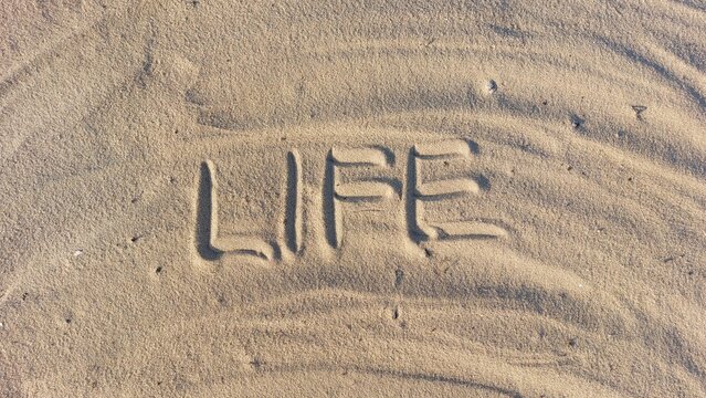 The word Life is written in the sand on the beach