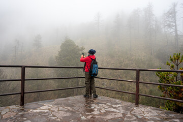 Tourist man in red coat is looking at the misty forest. Wanderlust travel concept, space for text, atmospheric epic moment, Nevado de Colima.