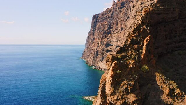 Aerial view reveal of mountains on the blue ocean in Tenerife, Canary islands, Spain. Clear morning sky. Los Gigantes cliffs. Huge barren rocks. Tranquil deep azure Atlantic waters.