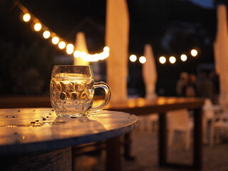 Fototapeta Kufel staojący na okrągłym stoliku, noc, światła lampek, złożone parasole,  obraz