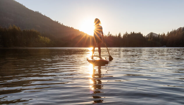 Adventurous Woman Paddling on a Paddle Board in a peaceful lake. Sunny Sunset. Hicks Lake, Sasquatch Provincial Park near Harrison Hot Springs, British Columbia, Canada.