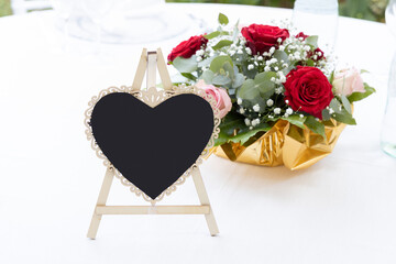 Segnaposto a forma di cuore e bouquet di fiori su un tavolo coperto da una tovaglia bianca, primo...