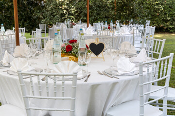 Tavolo apparecchiato per un pranzo di nozze, sedie, tovaglia, piatti bianchi e segnaposto a forma di cuore