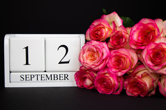 September 12 wooden calendar, white on a black background, pink roses lie nearby.Postcard with copy space. The concept of a holiday, congratulation, invitation, party, announcement, vacation,promotion