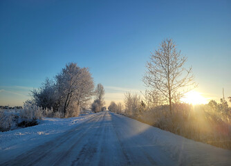 Fototapeta na wymiar Zima, słońce oświetla ośnieżoną drogę.