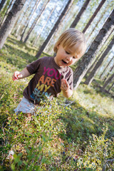 Blond Baby girl collecting berries in the forest and eating them