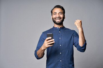Happy indian business man investor winner using cell mobile phone isolated on gray background....